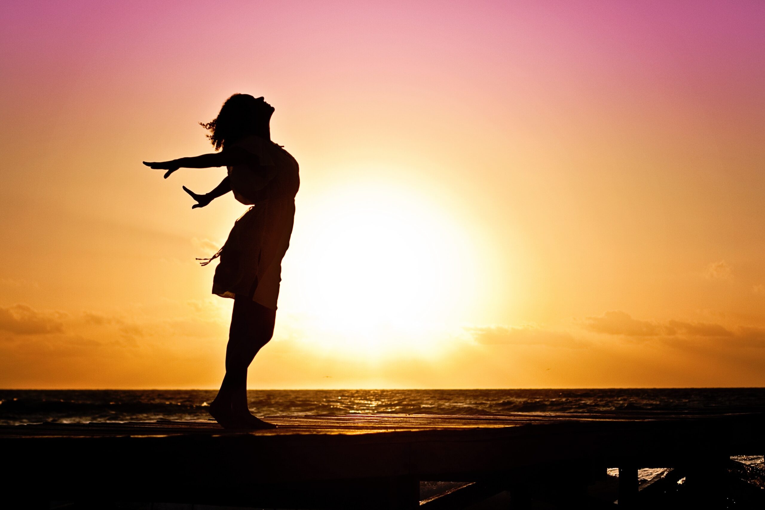 silhouette of a person standing on a pier at sunset