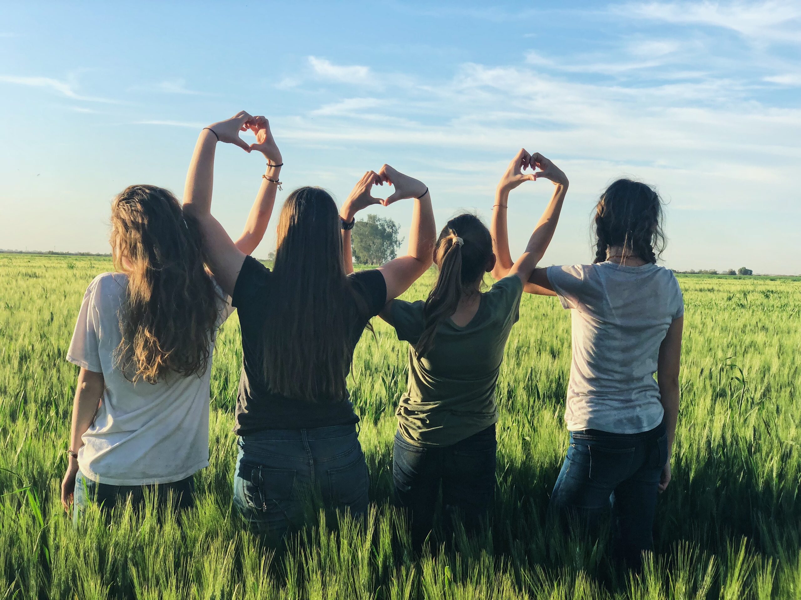 four people making heart shapes with their hands in a green field