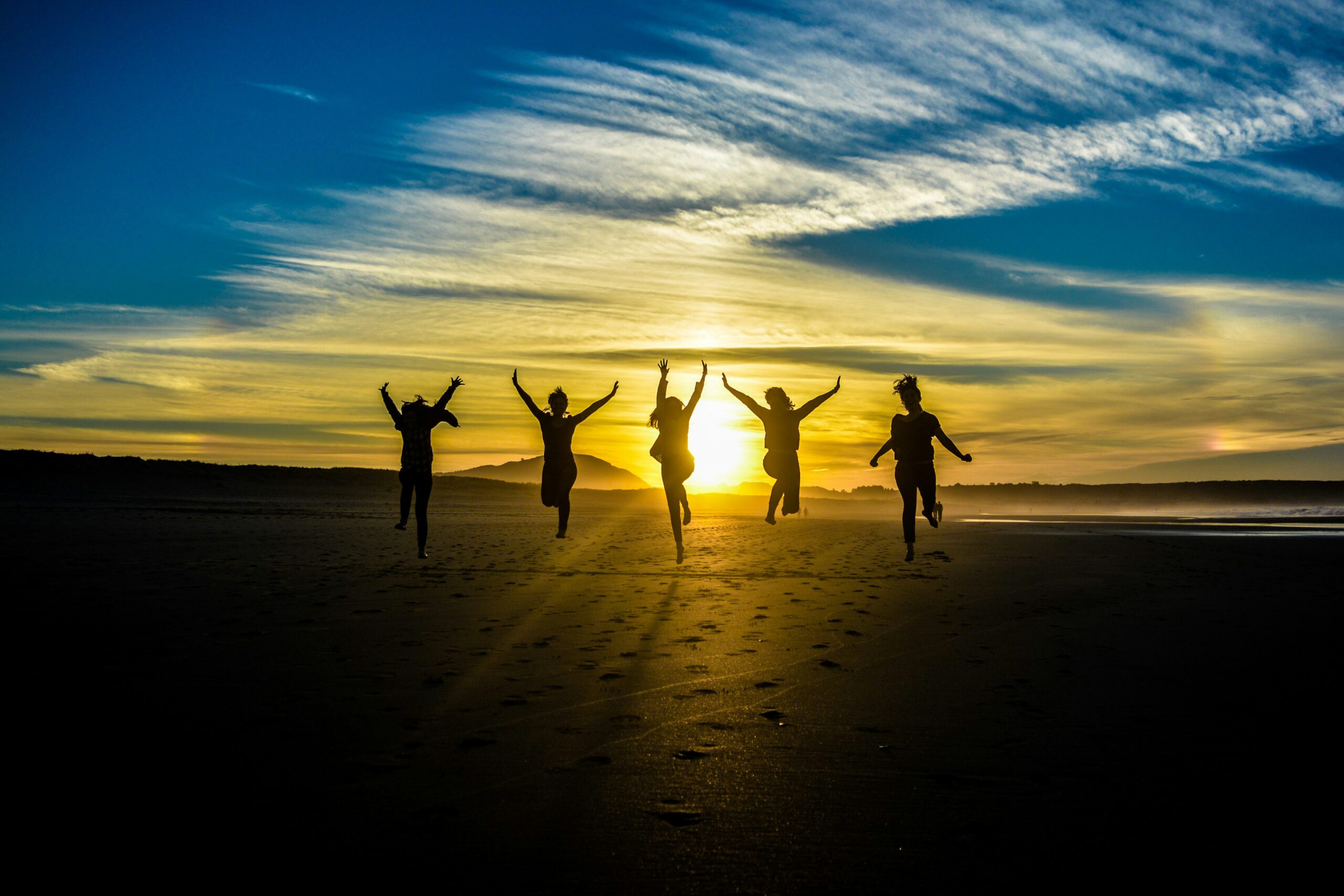 five silhouetted figures jump joyfully on a beach at sunset